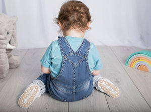 Baby boy sitting wearing a pair of stay-on baby booties featuring an elephant print on white cotton fabric, with non-slip soles and adjustable three snap closure. Made from organic cotton.