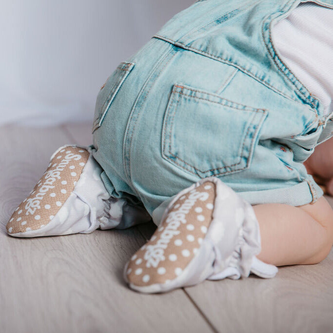Baby crawling wearing a pair of neutral grey stay-on organic cotton baby booties, with non-slip soles and adjustable three snap closure. Barefoot baby shoes. Pram slippers for babies