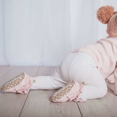 Baby girl crawling wearing a pair of Snugabugz pink baby booties  that stay on featuring a white heart print on organic cotton velvet fabric, with anti-slip soles and adjustable snap closure.  organic cotton pram slippers. beautiful baby shower gift