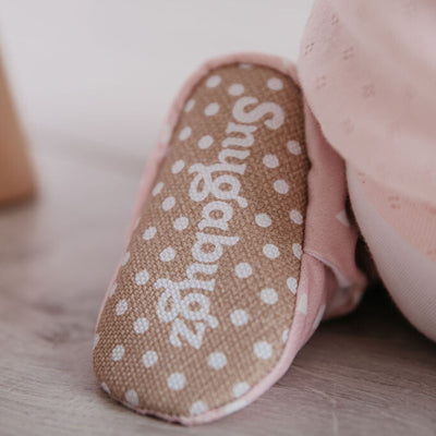 close up shot of Snugabugz stay-on baby girl booties featuring a white hearts print on a pink background, with non-slip soles and adjustable popper closure. Pram shoes made from organic cotton. new baby girl gift