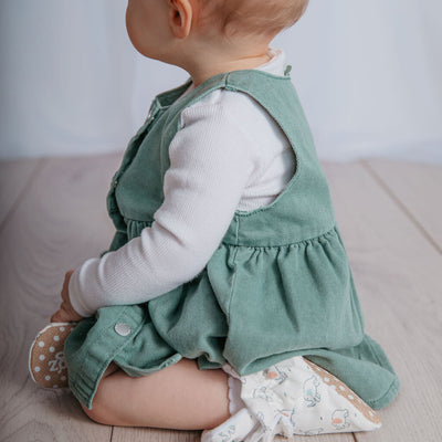 Baby girl playing wearing a pair of Snugabugz stay-on baby booties featuring a neutral elephant print on a white background, with non-slip soles and adjustable three snap closure. Made from organic cotton.