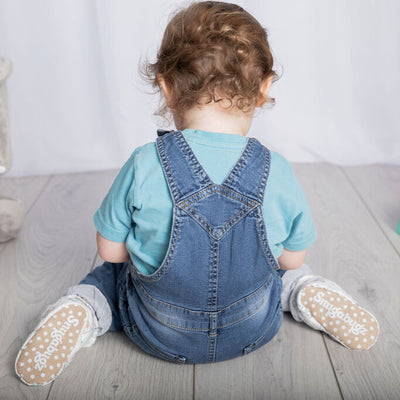 Baby boy playing wearing a pair of Snugabugz stay-on baby booties featuring a neutral elephant print on a white background, with non-slip soles and adjustable three snap closure. Made from organic cotton.